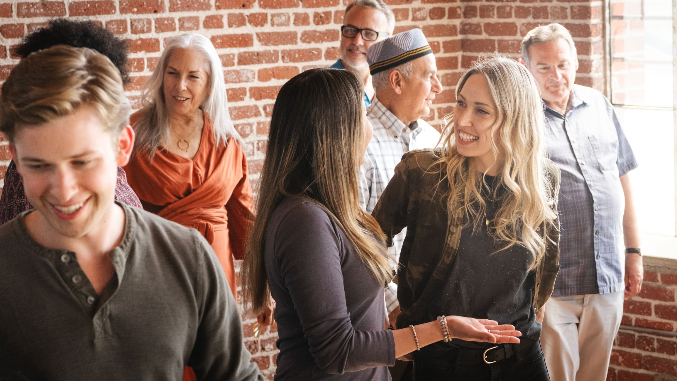 Group of diverse people socializing indoors. Smiling men and women, various ages, enjoying conversation. Casual gathering, friendly atmosphere, brick wall. Diverse group of people at social event.