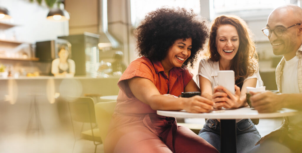 Group of friends having fun and making a video call, enjoying coffee and wi-fi at a local café. Happy young people hanging out together over a social lunch on the weekend.